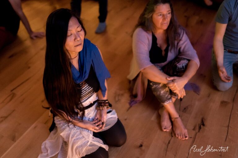 Zwei Frauen in meditativer Pose auf einem Holzfußboden, umgeben von einer entspannten Atmosphäre – © Axel Hebenstreit