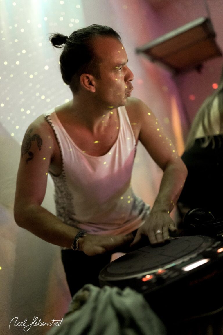 Ein DJ spielt mit Leidenschaft an einem Musik-Setup in einer stimmungsvollen, lichtdurchfluteten Umgebung – © Axel Hebenstreit