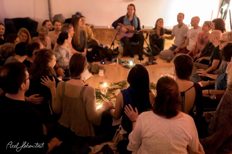 Eine Gruppe von Menschen sitzt im Kreis, um eine musikalische Darbietung in einem gemütlichen Raum zu erleben – © Axel Hebenstreit