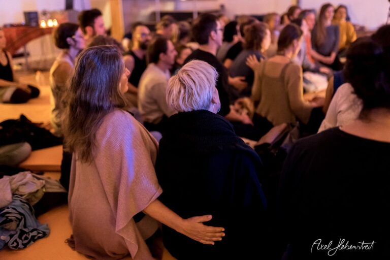 Eine Gruppe von Menschen sitzt in einem meditativen Moment zusammen, umgeben von sanftem Licht – © Axel Hebenstreit