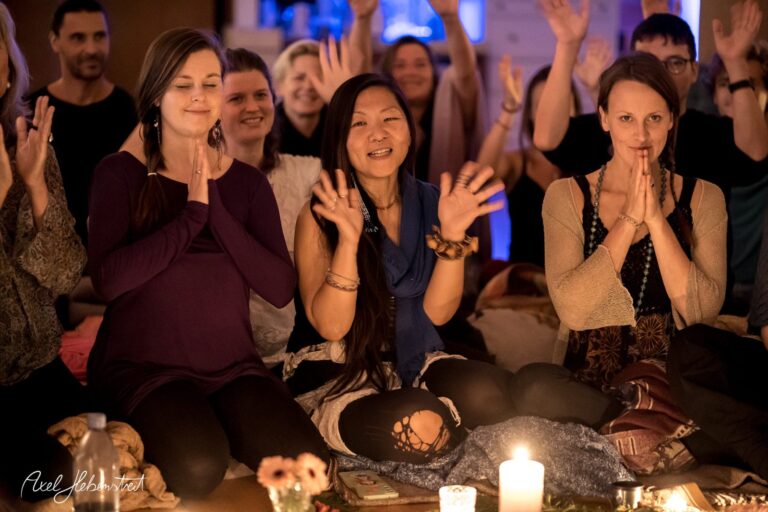 Eine Gruppe von Menschen sitzt gemeinsam in einer meditativen Atmosphäre, Hände zusammen in Dankbarkeit gehoben – © Axel Hebenstreit