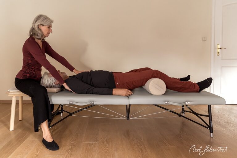 Eine Frau gibt einem Mann auf einer Massageliege eine Behandlung in einem hellen, ruhigen Raum – © Axel Hebenstreit.