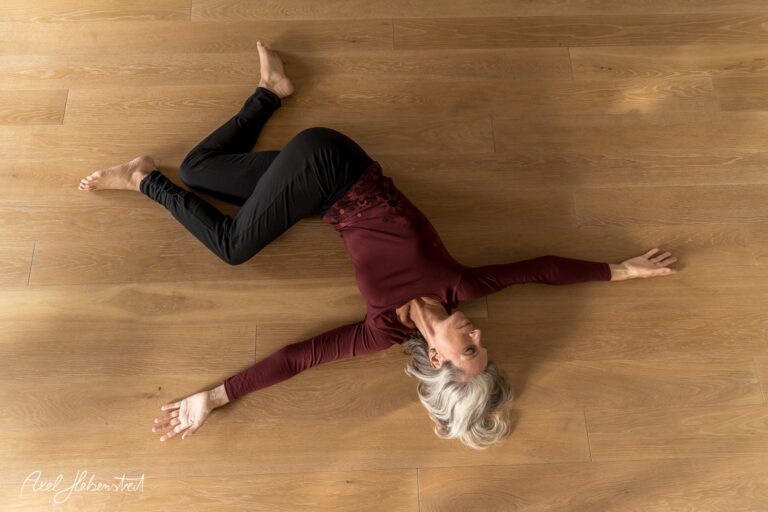 Eine Frau in yogischer Pose liegt entspannt auf einem Holzboden – © Axel Hebenstreit.