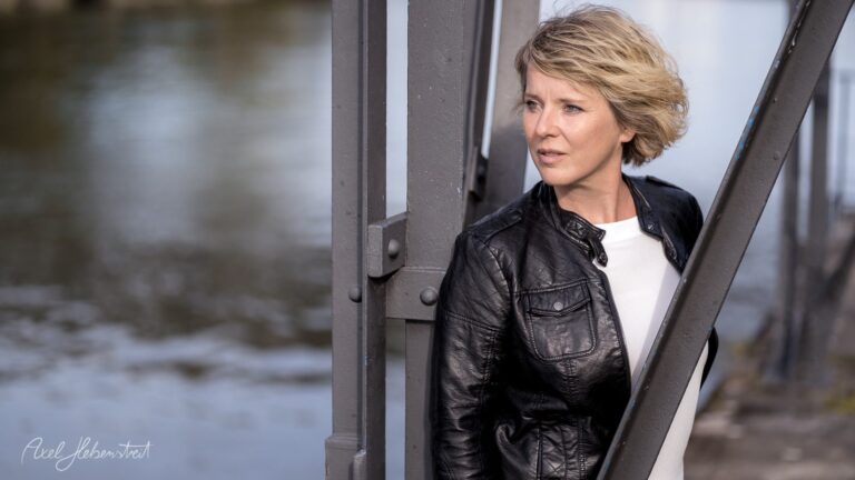 Dramatisches Portrait einer Frau in Lederjacke am Ufer eines Gewässers mit nachdenklichem Ausdruck – © Axel Hebenstreit