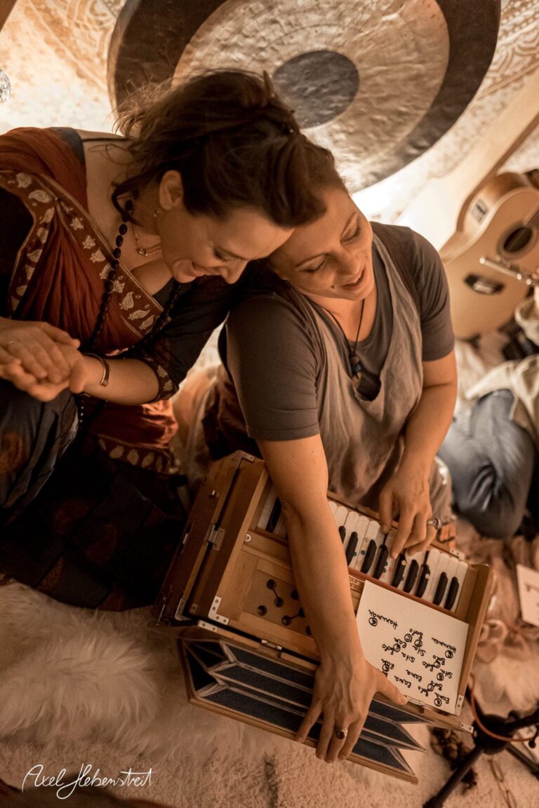 Zwei Frauen sitzen harmonisch zusammen und spielen auf einem Harmonium in einer warmen, einladenden Umgebung – © Axel Hebenstreit