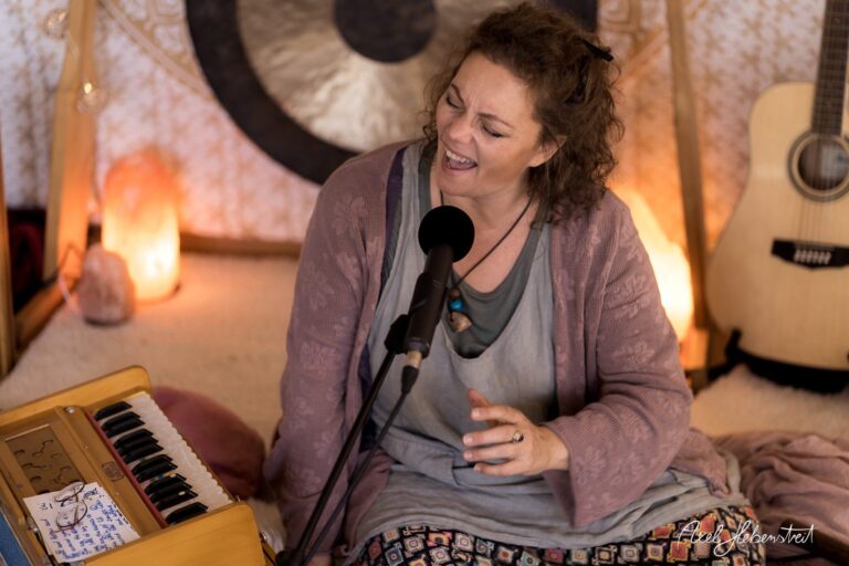 Eine Musikerin singt leidenschaftlich in einer gemütlichen Umgebung, umgeben von sanften Lichtquellen und Musikinstrumenten. – © Axel Hebenstreit