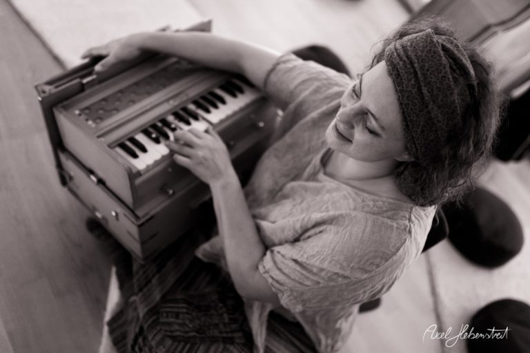 Eine Frau spielt fröhlich auf einem kleinen Keyboard in einer entspannten Yoga-Umgebung – © Axel Hebenstreit.