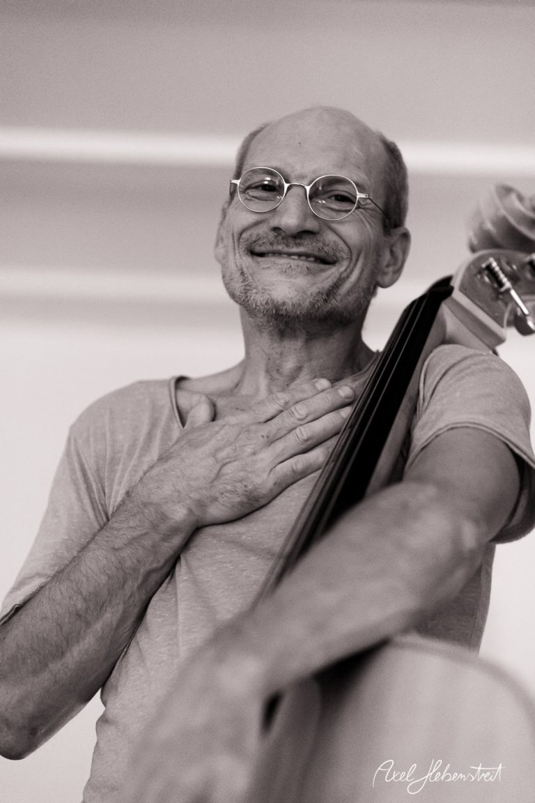 Ein lächelnder Mann mit Brille umarmt sein Cello und strahlt Freude aus. – © Axel Hebenstreit