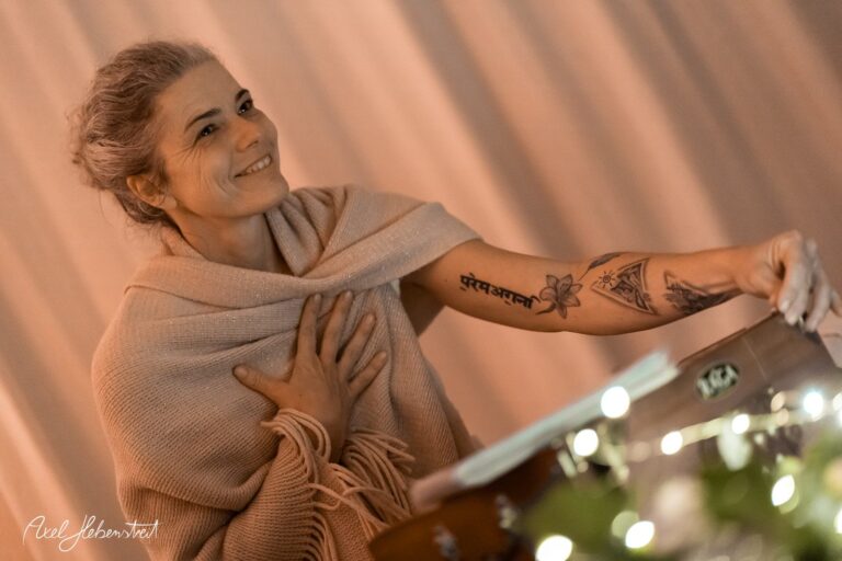 Eine lächelnde Frau mit einem Tattoo auf dem Arm umarmt die Musik in einer warmen, stimmungsvollen Umgebung – © Axel Hebenstreit