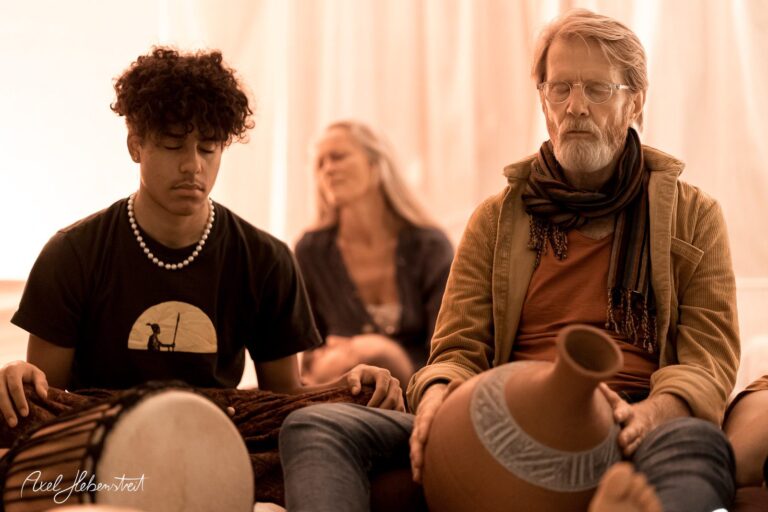 Junge und ältere Männer meditieren während einer spirituellen Session, umgeben von sanfter Beleuchtung – © Axel Hebenstreit