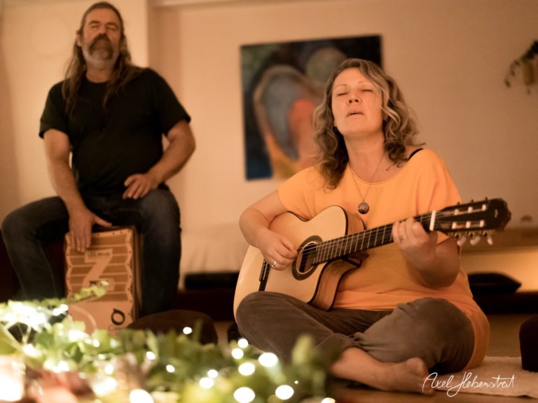 Musiker spielen live in gemütlicher Atmosphäre, während eine Frau auf der Gitarre singt – © Axel Hebenstreit