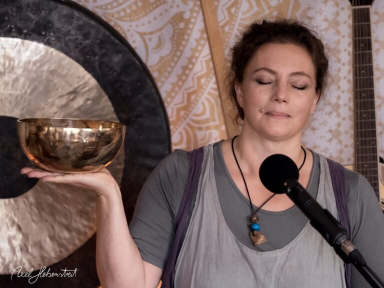 Frau mit verschlossenen Augen hält eine Klangschale in der Hand, umgeben von einer meditativen Atmosphäre – © Axel Hebenstreit