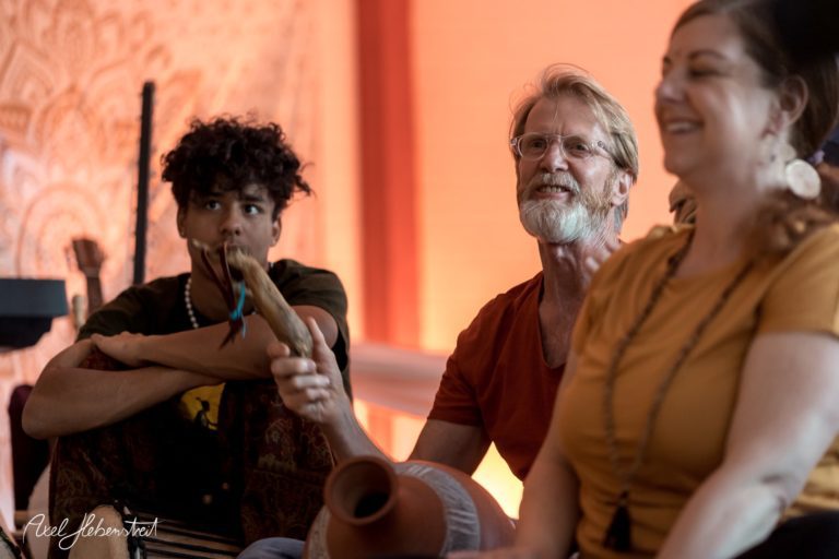 Eine Gruppe von Menschen sitzt entspannt zusammen, während sie Musikinstrumente halten und lachen – © Axel Hebenstreit.