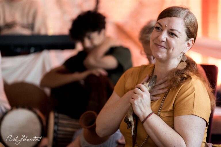 Eine lächelnde Frau in einem gelben Kleid hält eine kleine Figur in der Hand und strahlt positive Energie aus – © Axel Hebenstreit