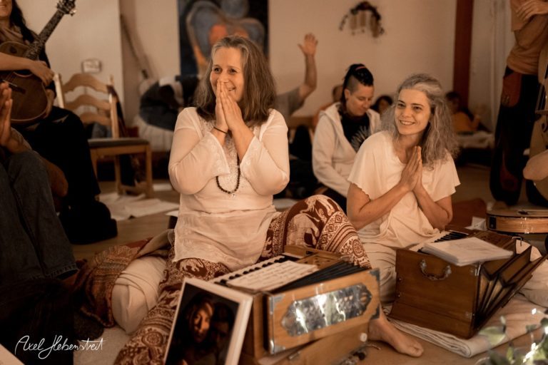 Zwei Frauen im Sitzen, lächeln und fügen sich in eine entspannte, meditative Atmosphäre während einer Yogaveranstaltung – © Axel Hebenstreit