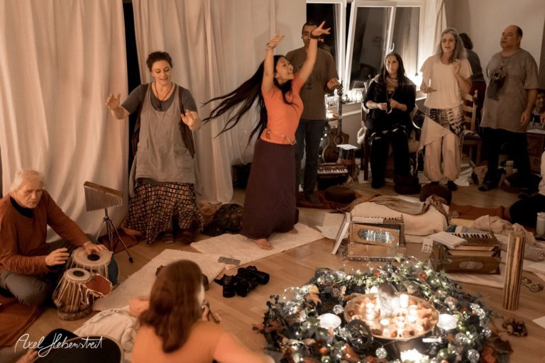 Eine spirituelle Versammlung mit tanzenden und musizierenden Menschen in einem warmen, einladenden Raum – © Axel Hebenstreit