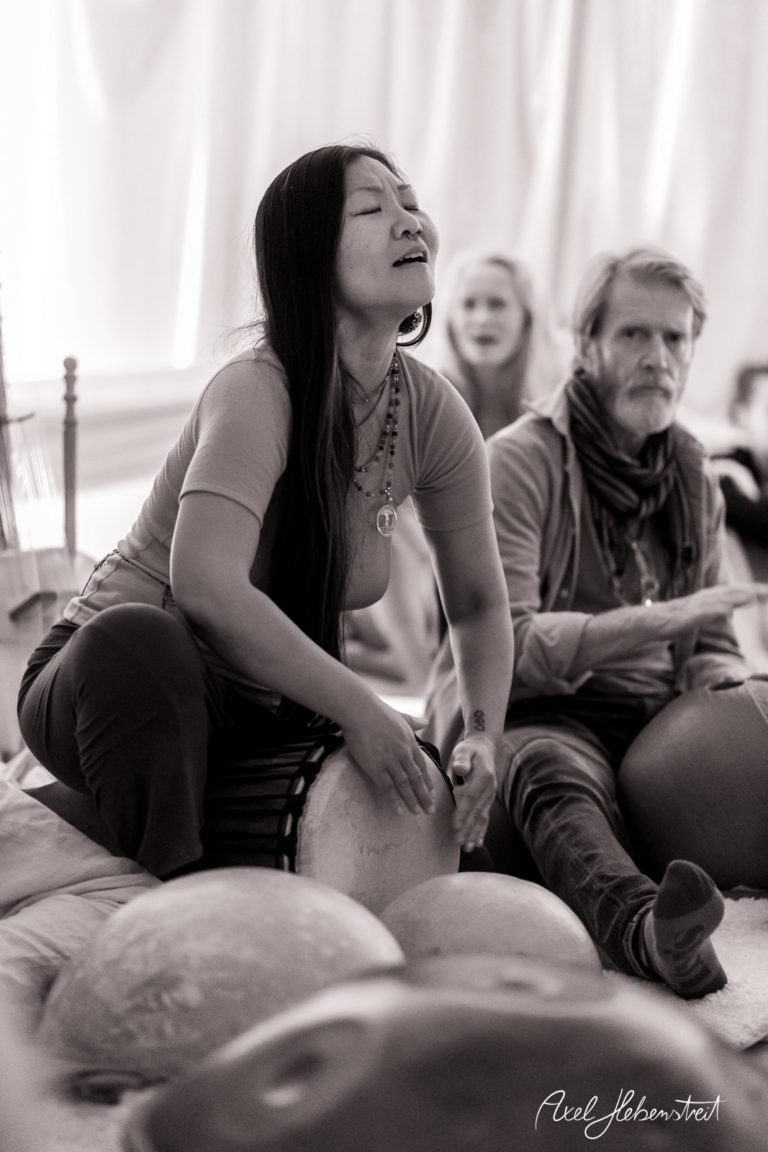Eine Frau sitzt in meditativer Stimmung und spielt ein Musikinstrument, während ein Mann daneben aufmerksam lauscht – © Axel Hebenstreit