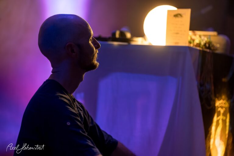 Ein meditativer Moment eines Mannes im Profil vor einer beleuchteten Kulisse auf einem Festival – © Axel Hebenstreit