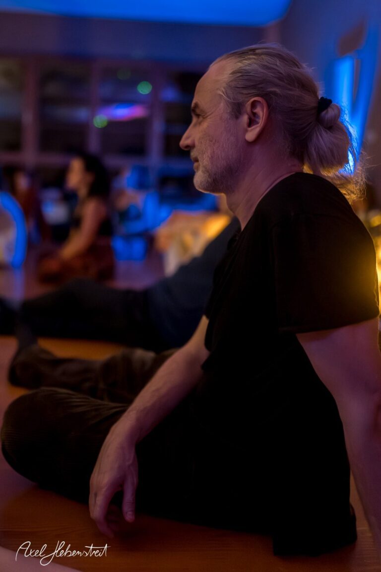 Mann im Lotussitz während einer entspannten Yoga-Session in einem atmosphärisch beleuchteten Raum – © Axel Hebenstreit
