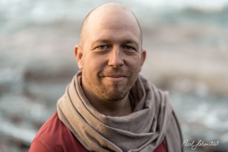 Lächelnder Mann mit einem Schal vor unscharfem Hintergrund am Wasser – © Axel Hebenstreit