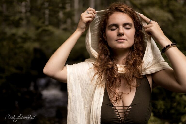 Porträt einer rothaarigen Frau mit weißem Tuch vor grünem Waldgrund – © Axel Hebenstreit