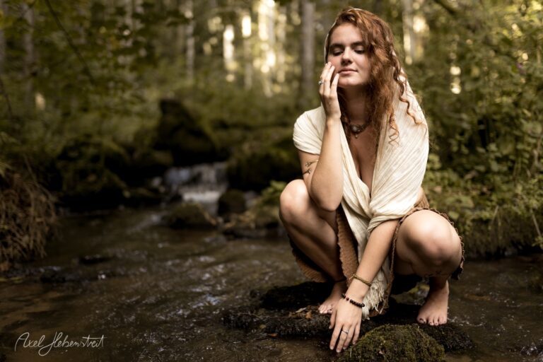 Junge Frau mit rötlichen Haaren sitzt nachdenklich in einem moosigen Waldbach – © Axel Hebenstreit