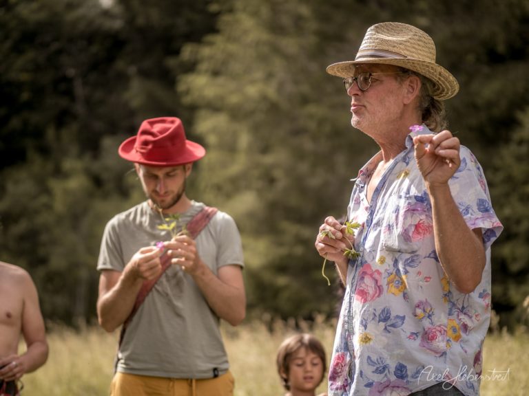 Mann in Blumenshirt und Strohhut zeigt Blume bei Naturveranstaltung im Freien – © Axel Hebenstreit