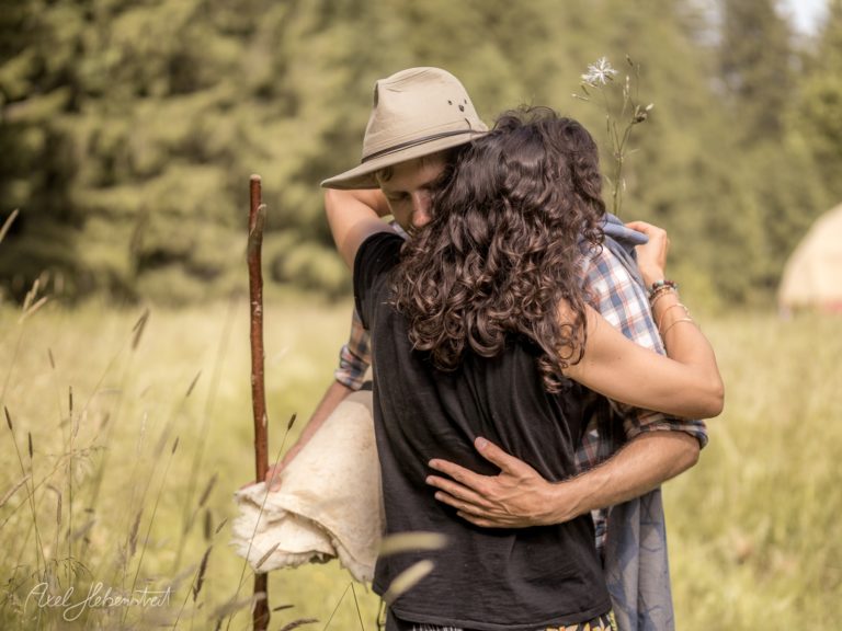 Mann im Cowboyhut trägt Frau mit langen braunen Haaren auf den Armen in idyllischer Naturlandschaft – © Axel Hebenstreit