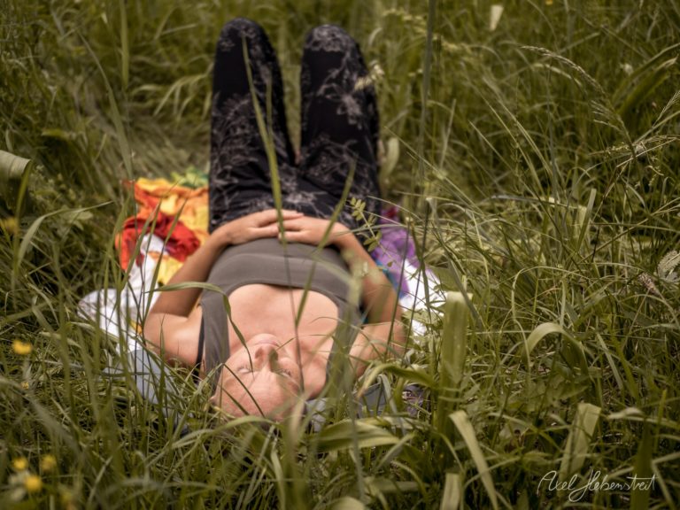 Person liegt entspannt im hohen Gras einer Wiese mit buntem Picknick-Tuch – © Axel Hebenstreit