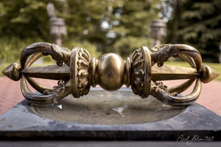 Ornamentales Bronzetor mit Löwenköpfen und Kugel in klassischem Parkgarten mit verschwommenem Hintergrund – © Axel Hebenstreit