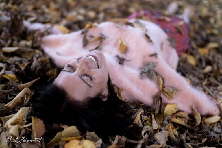 Lächelnde Frau liegt im Herbstlaub und genießt die Natur – © Axel Hebenstreit