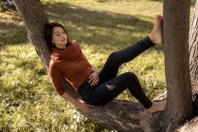 Junge Frau entspannt in einem Baum im Grünen, mit einem nachdenklichen Ausdruck und barfuß sitzend – © Axel Hebenstreit