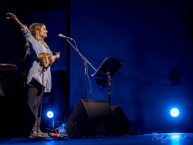 Eine Sängerin steht auf der Bühne, hebt die Arme und begeistert das Publikum mit ihrer Musik. – © Axel Hebenstreit