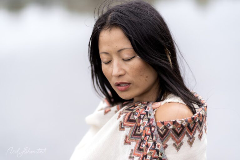 Porträt einer Frau in traditionellem Strickpullover mit geometrischem Muster, nachdenklicher Blick nach unten vor unscharfem Hintergrund – © Axel Hebenstreit