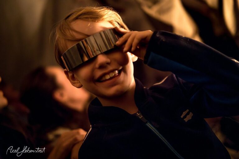 Ein fröhlicher Junge mit futuristischen Sonnenbrillen lächelt und posiert in einer festlichen Atmosphäre – © Axel Hebenstreit