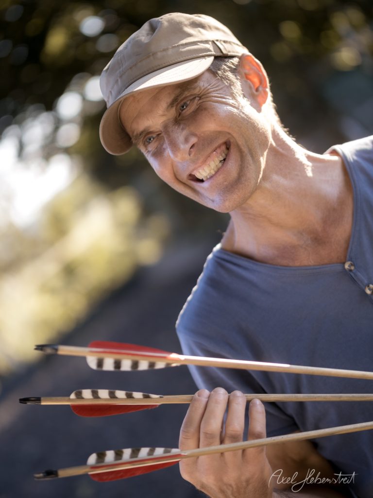 Lächelnder Bogenschütze mit Pfeilen in der Hand beim Sporttraining im Freien – © Axel Hebenstreit