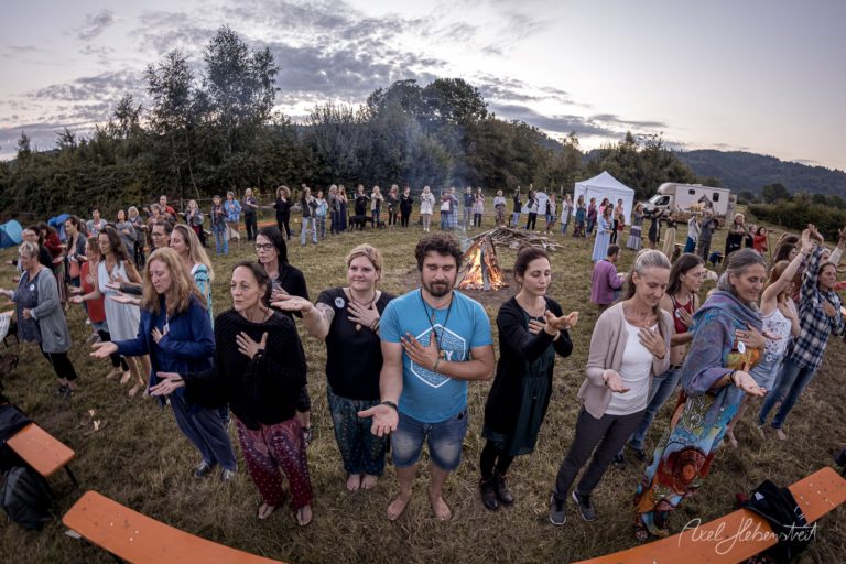 Große Gruppe von Menschen tanzt und feiert bei Sonnenuntergang auf einer Wiese in den bayerischen Bergen – © Axel Hebenstreit