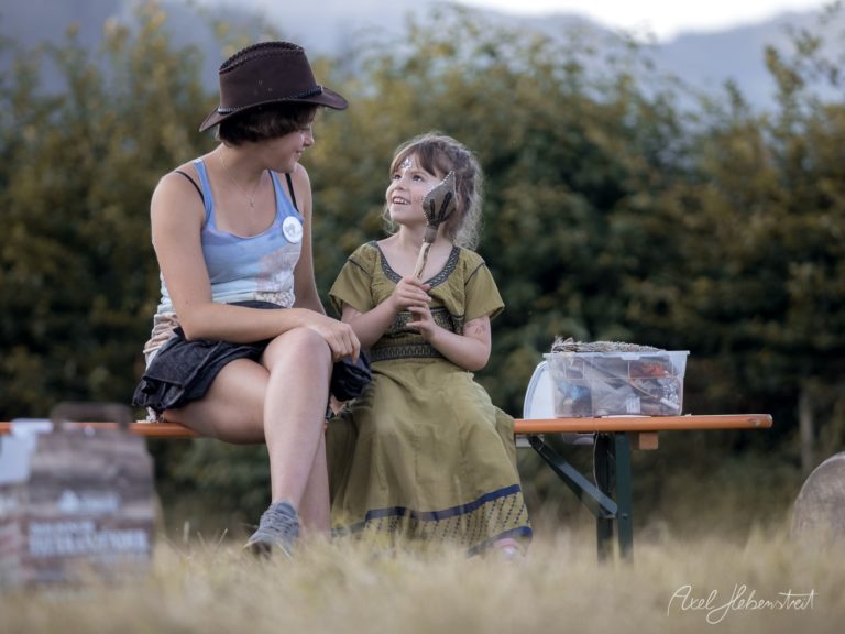 Zwei Frauen sitzen zusammen auf einer Bank in alpiner Berglandschaft und teilen einen glücklichen Moment – © Axel Hebenstreit
