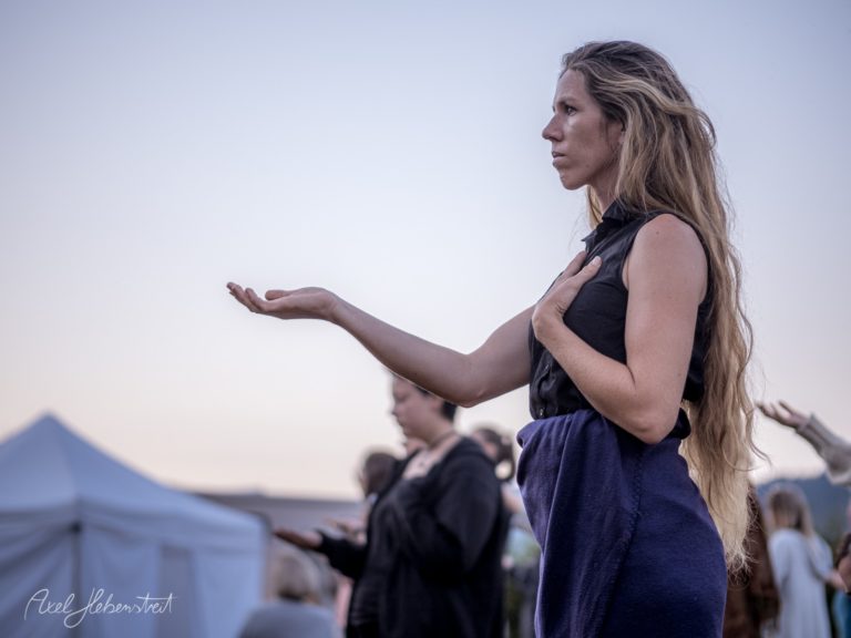 Frau mit langen Haaren gestikulierend auf Festivalgelände mit Zelt im Hintergrund – © Axel Hebenstreit