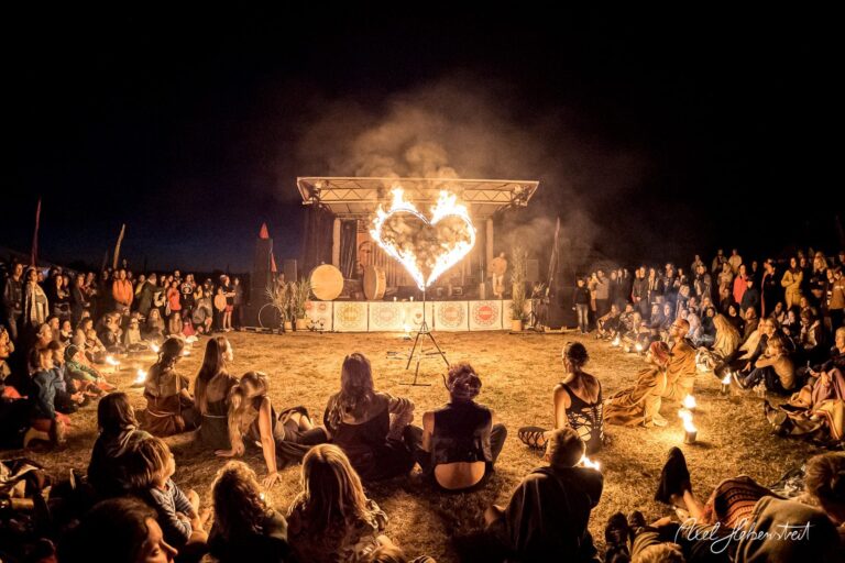 Die Zuschauer sitzen um eine Feuerperformance, während ein Herz aus Flammen in der Nacht leuchtet – © Axel Hebenstreit.