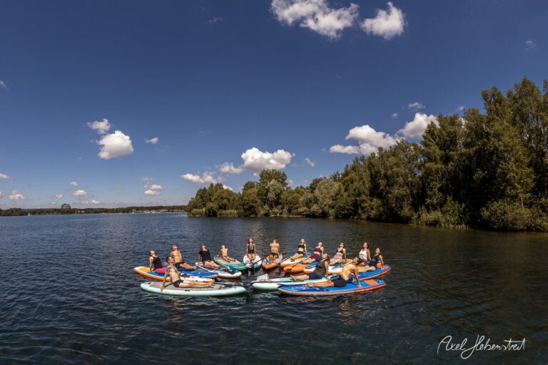 Gruppe von Menschen auf Stand-Up-Paddle-Boards in ruhigem Gewässer, umgeben von Natur – © Axel Hebenstreit