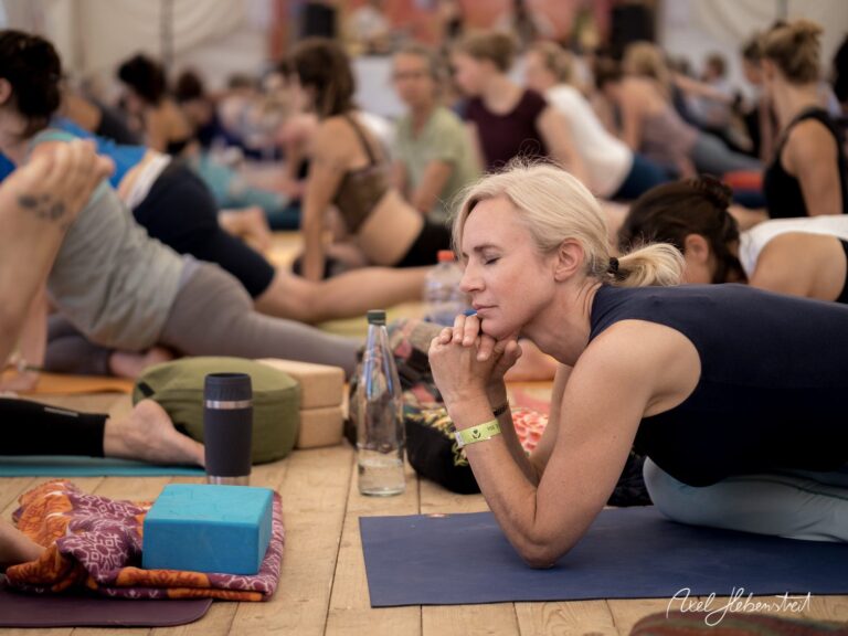 Eine Frau in yogischer Pose meditiert inmitten einer Gruppe in einem Festivalzelt – © Axel Hebenstreit.