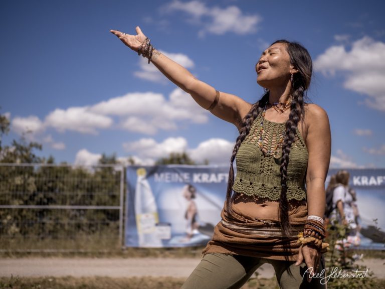 Frau in kreativer Pose im Freien, strahlt Freude und Lebensenergie während eines Festivals aus – © Axel Hebenstreit