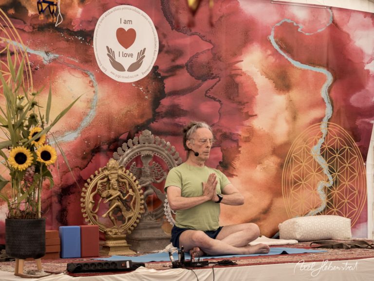 Ein meditierender Mann in einem Yogastudio vor einer bunten Wand mit spirituellen Symbolen – © Axel Hebenstreit