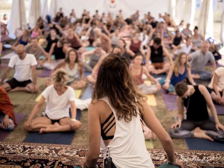 Eine Gruppe von Yoga-Teilnehmern praktiziert gemeinsam in einem Zelt während eines Retreats – © Axel Hebenstreit