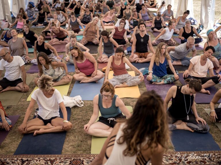 Eine große Gruppe von Menschen praktiziert Yoga in einem Zelt während eines Festivals. – © Axel Hebenstreit