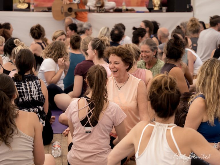 Eine fröhliche Gruppe von Menschen bei einer Yoga-Session, die sich in entspannter Atmosphäre austauschen – © Axel Hebenstreit