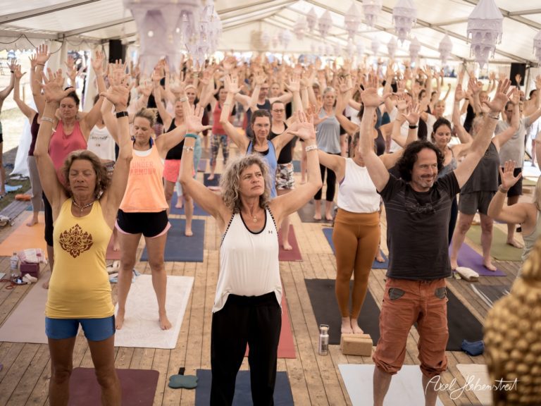 Gruppenyoga mit Teilnehmern in einer Zeltatmosphäre, die mit erhobenen Händen meditieren – © Axel Hebenstreit