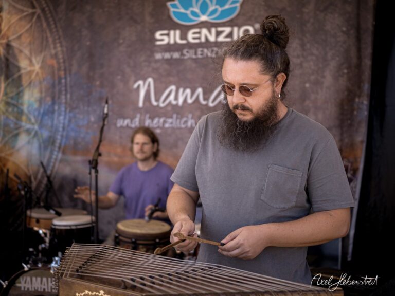 Musiker spielt auf einem Zither-ähnlichen Instrument bei einem Festival, während im Hintergrund ein Schlagzeuger zu sehen ist – © Axel Hebenstreit