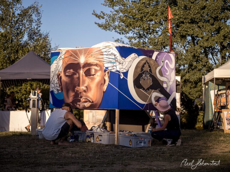 Zwei Künstler arbeiten an einem eindrucksvollen Wandgemälde auf einem Festivalgelände. – © Axel Hebenstreit